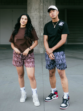 Load image into Gallery viewer, Our girl model wearing and representing our Monogram Logo Tee (Brown) combined with our Monogram Pattern Shorts (Brown) and our boy model wearing Monogram Logo Tee (Black), Monogram Pattern Shorts (Black) and our unreleased snapback hat.